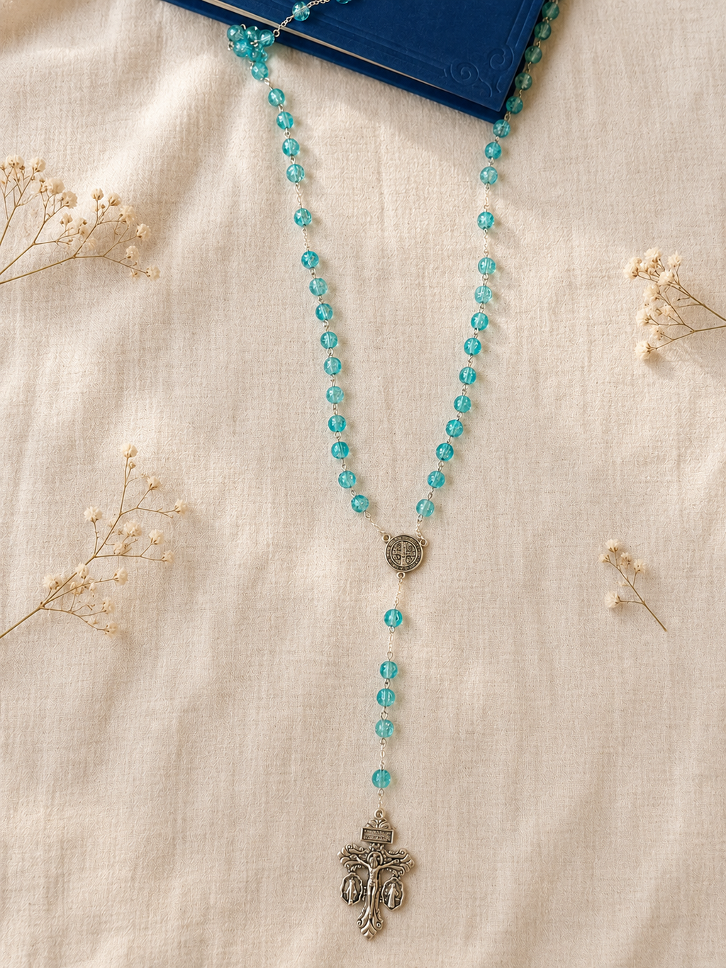 Turquoise beaded rosary with a silver pendant, Saint Benedict's medal and the 3-way Pardon Indulgence Crucifix on a beige fabric background